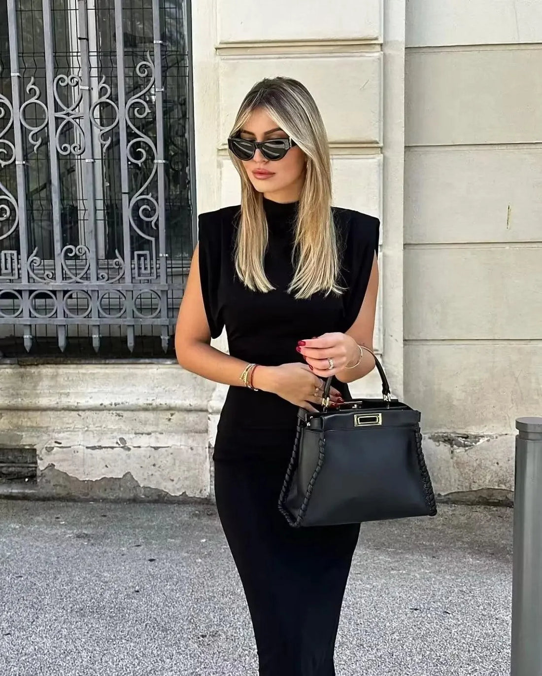 Femme en robe noire mi-longue à épaulettes avec un sac à main, look chic